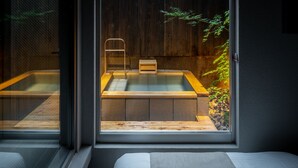 A modern room with a large window, a wooden bathtub, and a small wooden stool.
