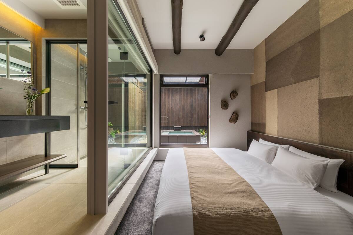 A modern hotel room with a large bed, a glass shower enclosure, a view of a pool, and a minimalist design.