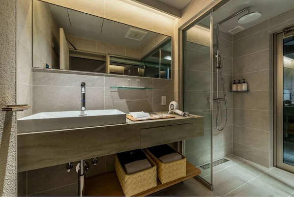 A modern bathroom with a large mirror, a sink, a shower, and storage baskets under the sink. - Nazuna Kyoto Tsubaki St. (Kyoto)