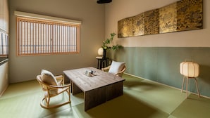 Ein traditioneller japanischer Raum mit Tatami-B öden, einem niedrigen Holztisch, zwei Tatami-Sesseln, einem Wandkunstwerk und einer Stehlampe.