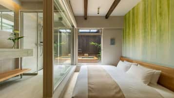 A modern hotel room with a large bed, a glass shower enclosure, a wooden bench, and a view of a pool and outdoor seating area.