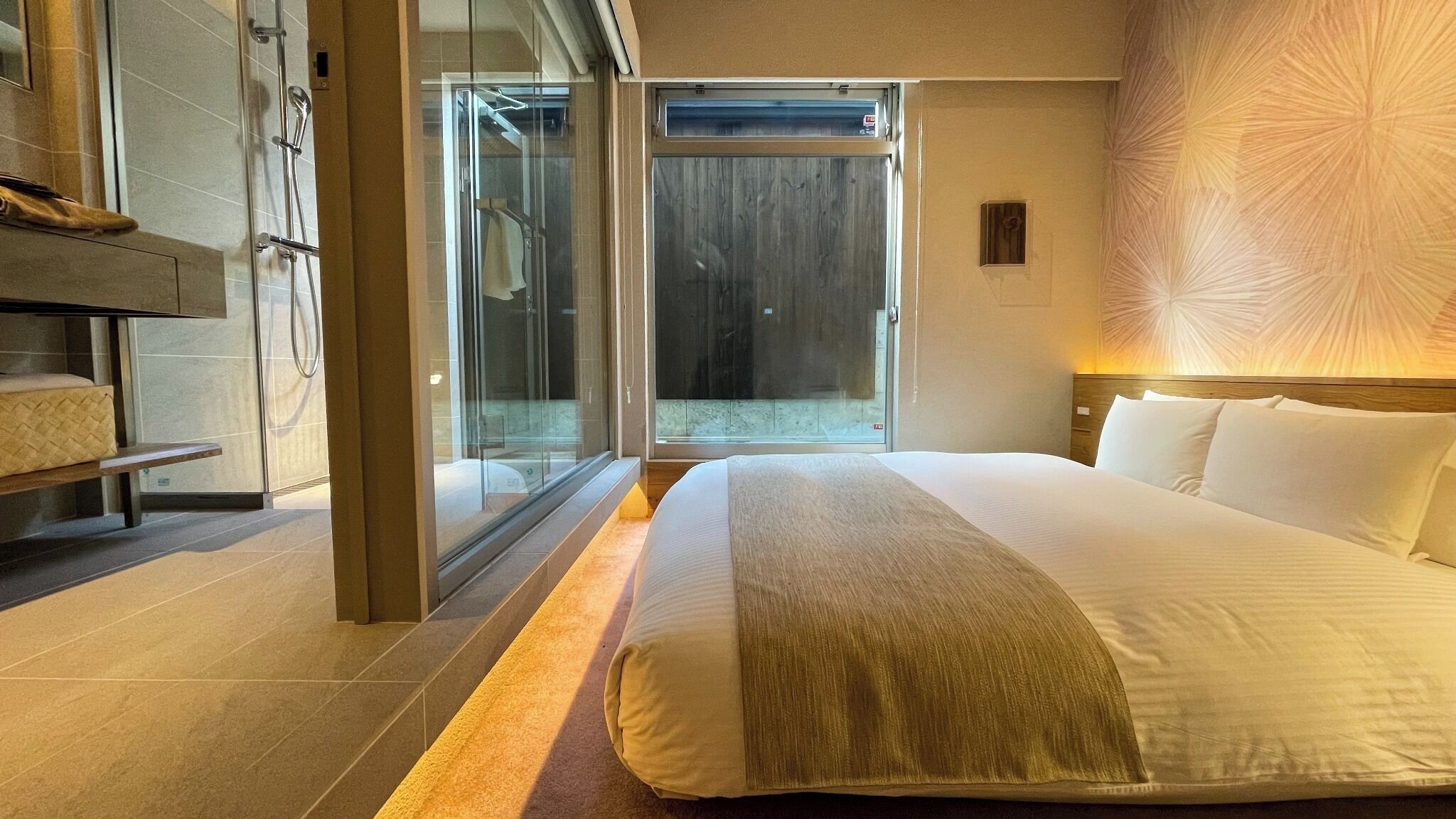 Een moderne hotelkamer met een groot bed, een bankje en een glazen deur naar een balkon.