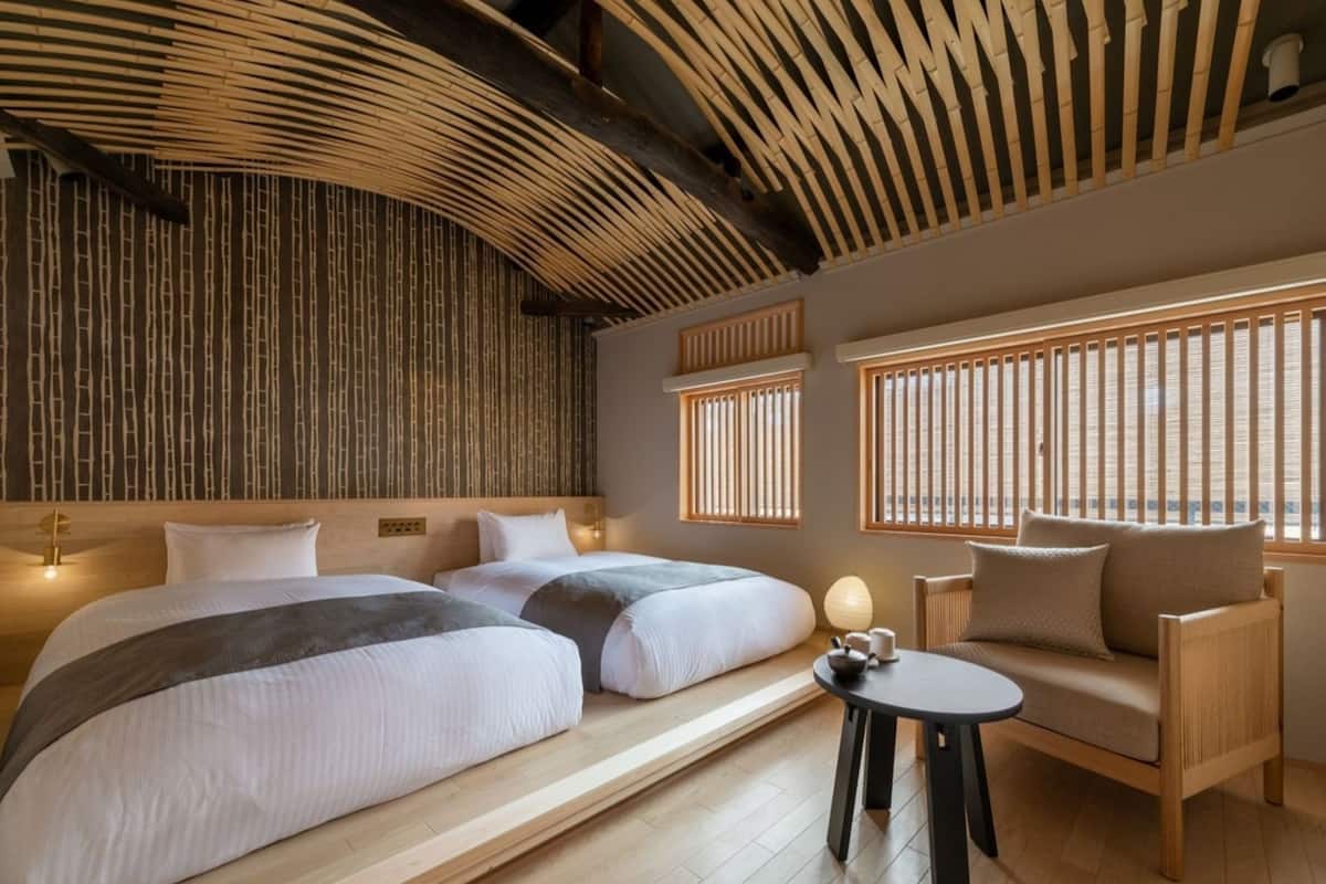 A hotel room with two beds, a sofa, a small table, and a view of the outside through large windows.