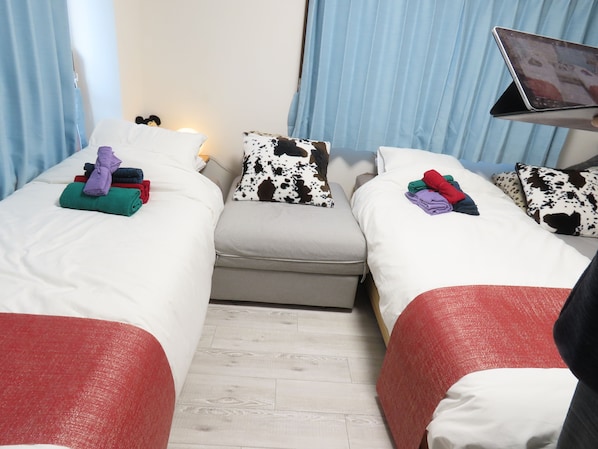 A hotel room with two beds, each with a pillow and a folded towel. There is a small table with a laptop and a lamp.