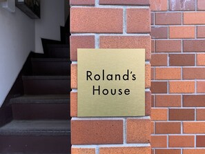 A brass plaque on a brick wall that reads "Roland's House".