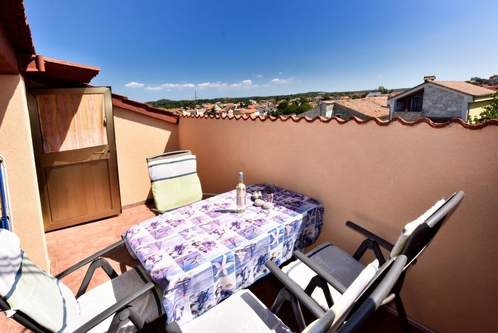 A balcony with a table and chairs, a wooden door, and a view of a town.