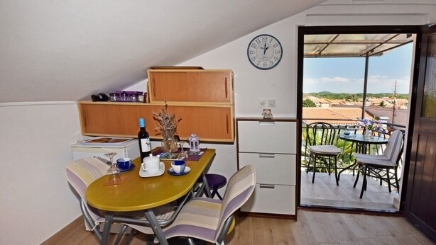 Een kleine keuken met een eethoek, een klok en uitzicht op het omliggende landschap door een geopende deur.