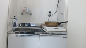 Une petite cuisine équipée d’un évier, d’un robinet et d’une plaque de cuisson mobile.