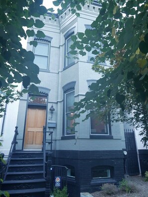 A two-story building with a dark front porch, a wooden door, and a black metal staircase leading to the entrance. - Slumber in Sophistication in Shaw-PKG (Washington)