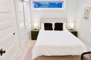 A bedroom with a large bed, two bedside tables, a window above the bed, and a door on the left. - Slumber in Sophistication in Shaw-PKG (Washington)