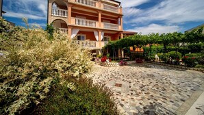 A two-story building with balconies, a courtyard with stone paving, and surrounding greenery. - Apartment in Lopar with Balcony, Air condition, WIFI, Washing machine (4886-2) (Lopar)