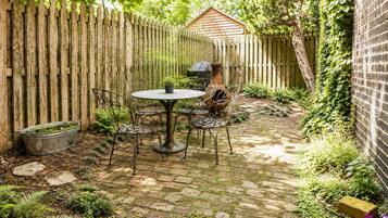 Eine Garten-Terrasse mit rundem Tisch und Stühlen, einem Metall-Pflanzgefäß und einer Ziegelmauer.