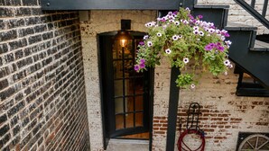 A brick building with a black door, a hanging flower basket, and a red hose on the ground. - Amazing Location - Close to Union Station (Washington)