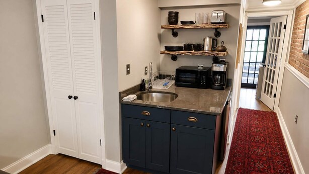 A kitchen with dark blue cabinets, a stainless steel sink, and a microwave. There are wooden shelves above the counter holding dishes and a coffee maker. - Amazing Location - Close to Union Station (Washington)