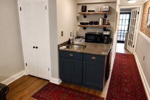 Une cuisine avec des meubles de couleur bleu foncé, un évier en acier inoxydable et un four à micro-ondes. Des étagères en bois sont fixées au-dessus du plan de travail et servent à ranger la vaisselle et un appareil à café.