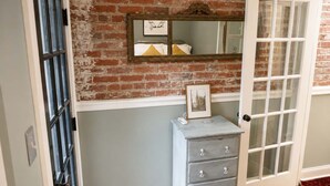 A room with a brick wall, a white door, a dresser with drawers, and a mirror on the wall. - Amazing Location - Close to Union Station (Washington)