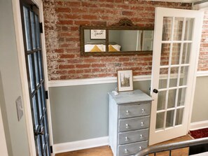 A room with a brick wall, a white door, a dresser with drawers, and a mirror on the wall. - Amazing Location - Close to Union Station (Washington)