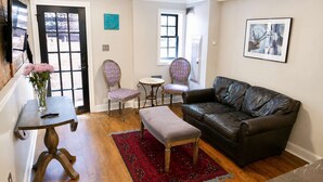 A living room with a leather sofa, two patterned chairs, a small round table, a red rug, and a vase with flowers. - Amazing Location - Close to Union Station (Washington)