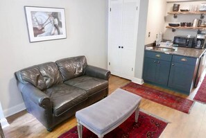 A living room with a leather sofa, a bench, a kitchen area with a microwave, and a red rug. - Amazing Location - Close to Union Station (Washington)