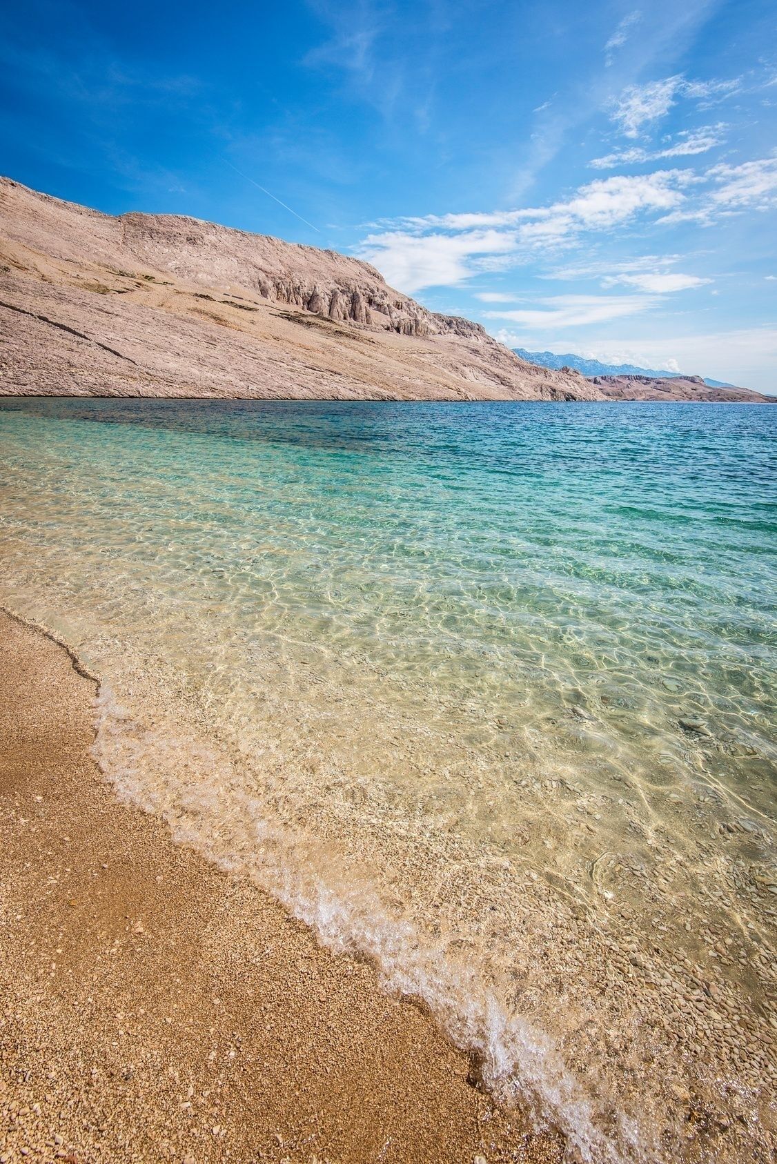 A clear beach with shallow water and a rocky shoreline.