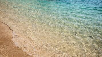 A clear beach with shallow water and a rocky shoreline.