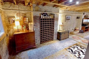 Una habitación rústica con paredes de ladrillo visto, un armario de madera, un botellero y una alfombra estampada.