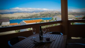 A wooden table with a bottle and glasses on a balcony overlooking a coastal town and mountains. - Apartment in Pag with Seaview, Terrace, Air condition, WIFI (4891-2) (Pag)