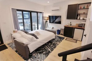 A hotel room with a bed, a desk, a flat-screen TV, a mini-fridge, and a kitchenette.