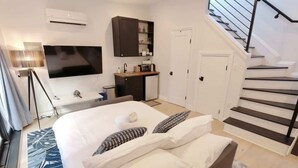 A bedroom with a bed, a TV, a small kitchenette, and a staircase.