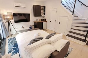 A bedroom with a bed, a TV, a small kitchenette, and a staircase.