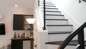 A staircase with black railings and white steps, a kitchen area with cabinets and a sink, and a floor lamp.