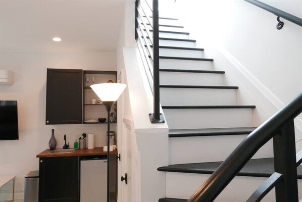 A staircase with black railings and white steps, a kitchen area with cabinets and a sink, and a floor lamp.