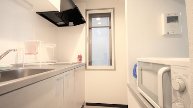 A compact kitchen with a stainless steel sink, a microwave, and a window. - Susukino Own It (Sapporo)