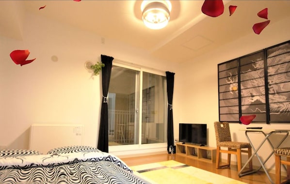 A hotel room with a bed, a desk with a chair, a TV, and a sliding glass door to the balcony.