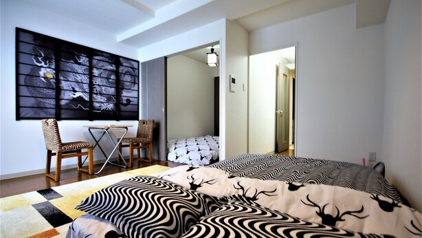 A bedroom with a bed, a desk, and a chair. There is a painting on the wall and a door leading to another room.