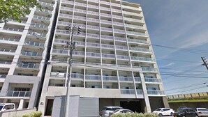 A multi-story residential building with balconies, a garage entrance, and parked cars.
