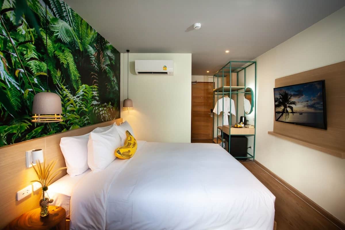 Quarto de hotel com cama, ar condicionado fixado na parede, um quadro e banheiro com chuveiro e porta-toalhas.