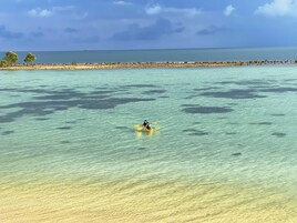 Um caiaque em um mar calmo e translúcido, com um navio ao longe e costa rochosa.