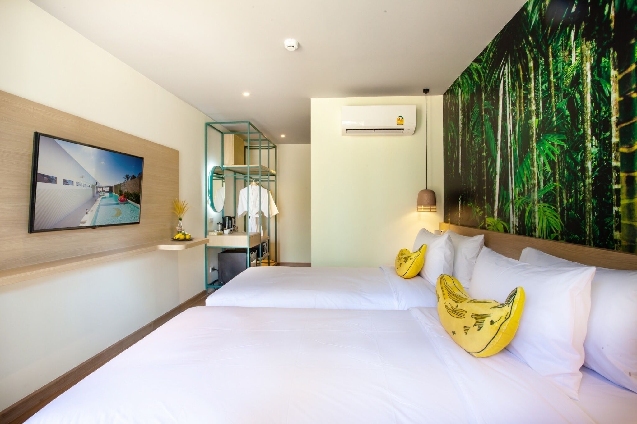 A hotel room with a large bed, a desk with a chair, a mounted TV, an air conditioner, and a large wall mural.