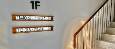 A staircase with wooden handrails and a white wall with apartment numbers 1406-1401 and 1306-1301 displayed.