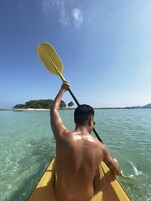 Una persona fa kayak su acque limpide, con una costa lontana e alberi.