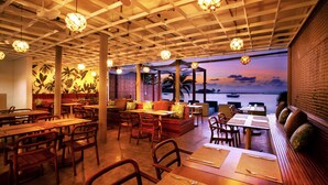 A restaurant with wooden tables and chairs, a seating area with cushions, and a view of the sea at dusk. - The Stay Chaweng Beach Resort (Koh Samui)