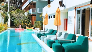 A poolside area with lounge chairs and umbrellas, a small inflatable boat, and a building with balconies and a sliding glass door. - The Stay Chaweng Beach Resort (Koh Samui)