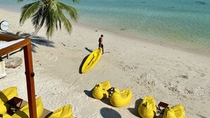 A beach with clear turquoise water, a palm tree, and yellow bean bags. - The Stay Chaweng Beach Resort (Koh Samui)