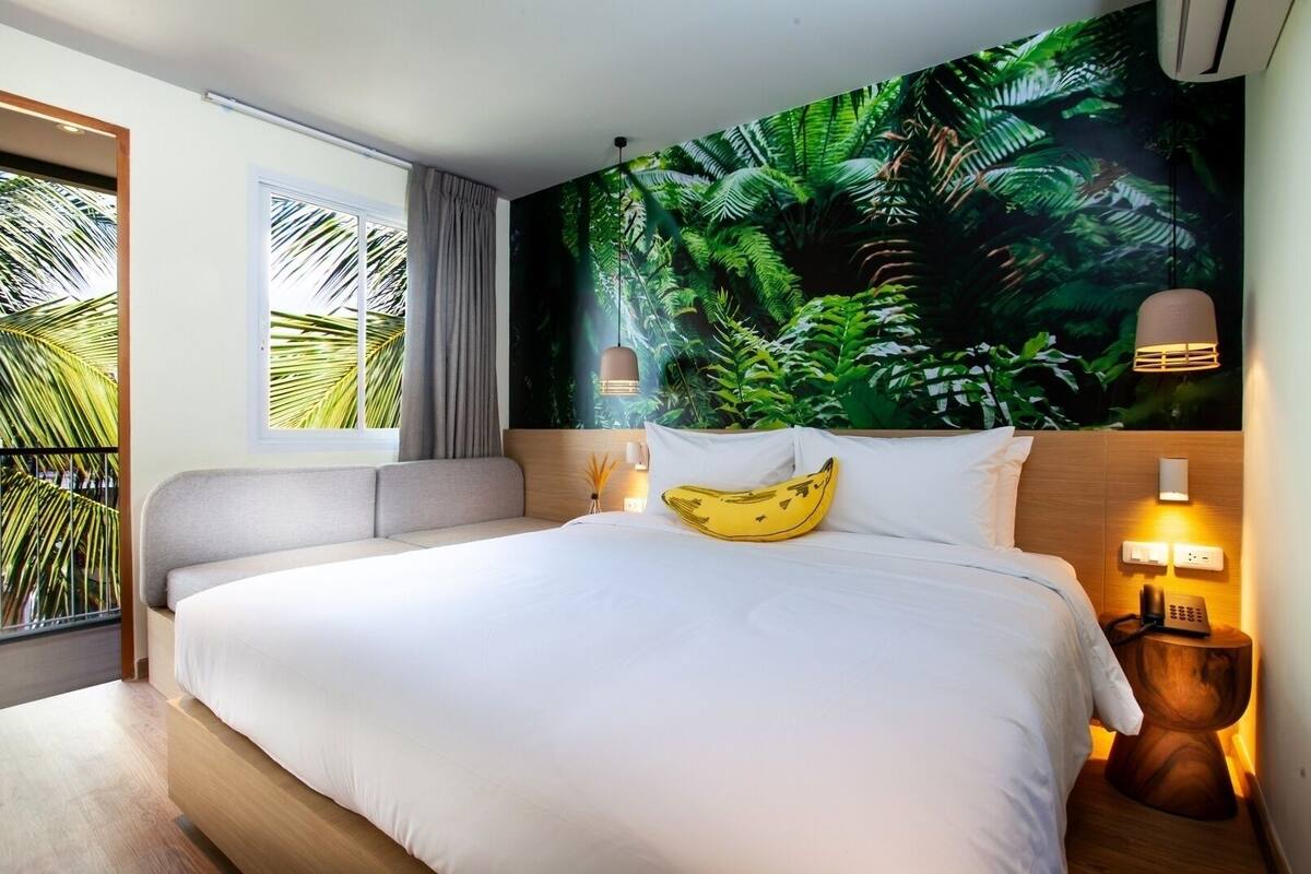 Quarto de hotel com uma cama grande, vista para palmeiras, um mural tropical e telefone ao lado da cama.