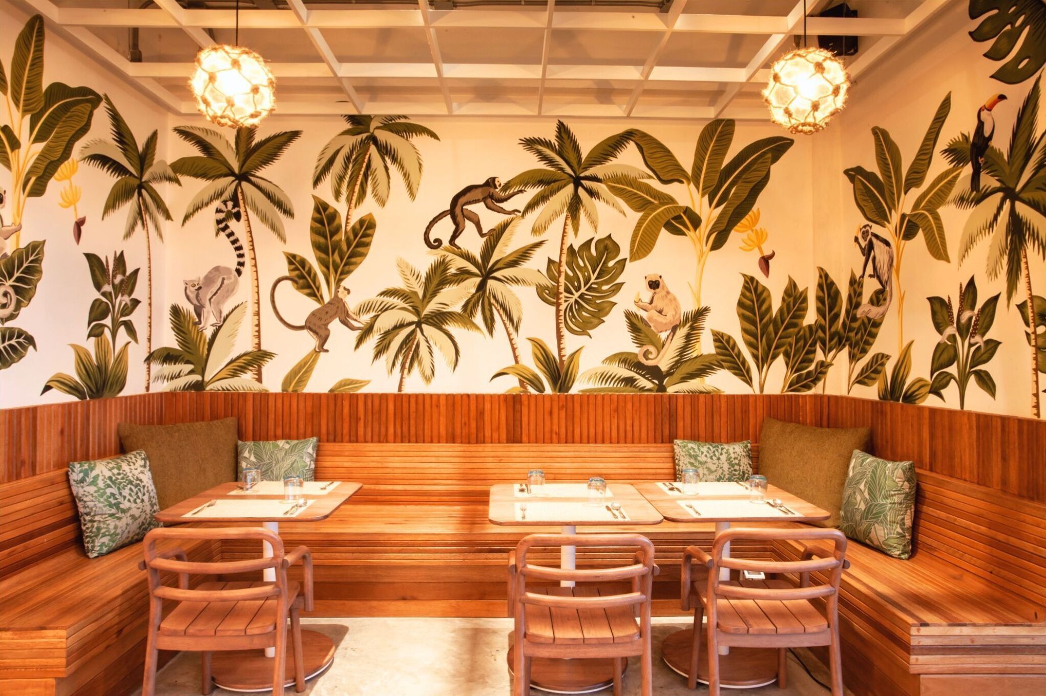 Un restaurant avec des sièges en bois, une longue table et une fresque murale représentant des plantes et des animaux tropicaux.