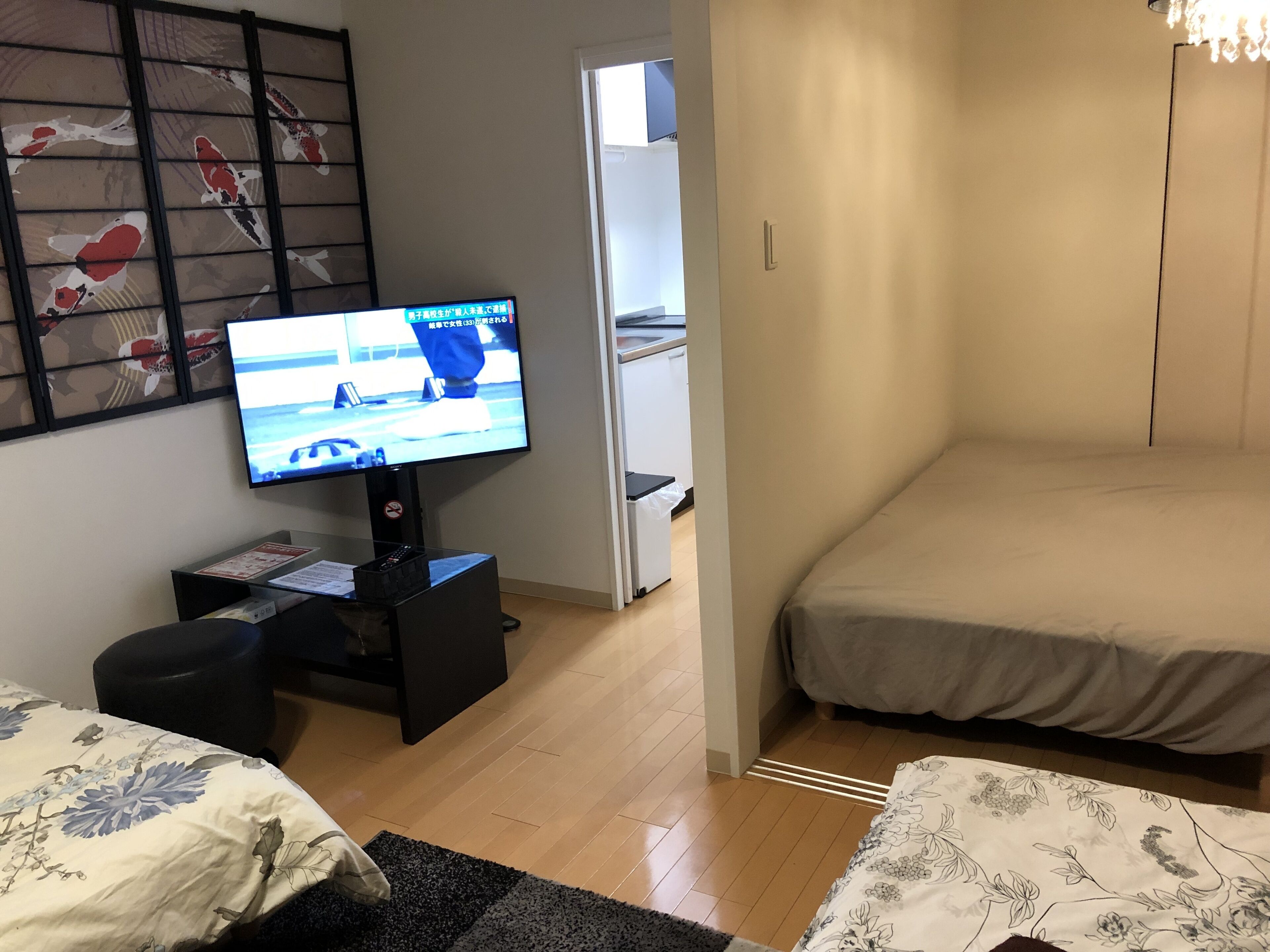 Een hotelkamer met een televisie op een standaard, een bed, een klein zithoekje met een stoel, en een houten vloer.