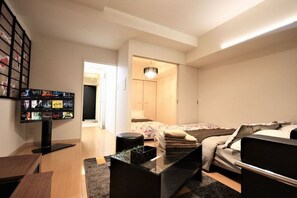 Una camera d'albergo moderna con una TV a schermo piatto, un letto con copripiumino floreale, un comodino con una pianta e un armadio a muro.