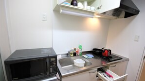 Una cocina compacta con microondas, pileta y una pequeña mesada.