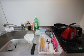 A kitchen counter with a sink, a red electric kettle, a black coffee maker, a white dish rack, and various kitchen utensils. - Irios Susukino 203 (Sapporo)